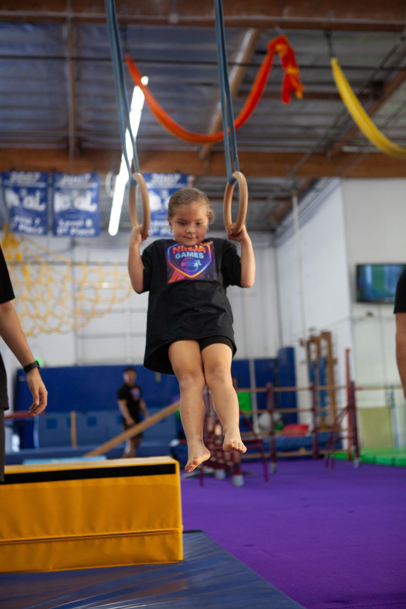 Young girl on gymnastic rings at a gym, with spotter.
