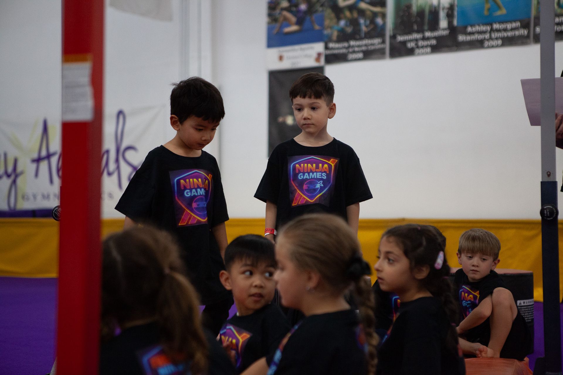 Children in black shirts at a gymnastics event.