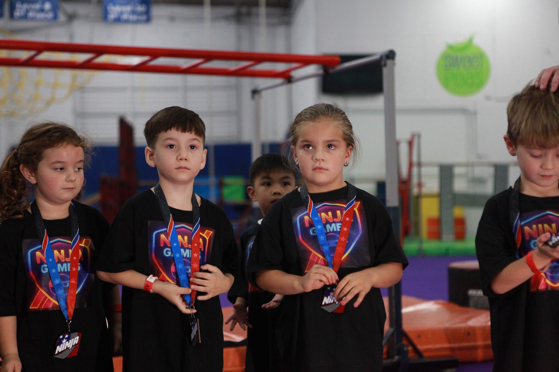 Children with medals at a ninja warrior gym; wearing black shirts.