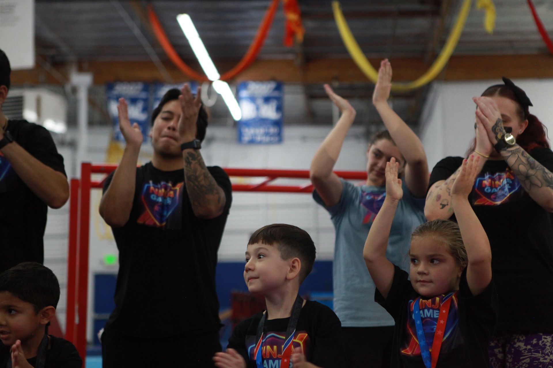 People clapping in an indoor gymnasium, celebrating with colorful streamers and a blue and white background.