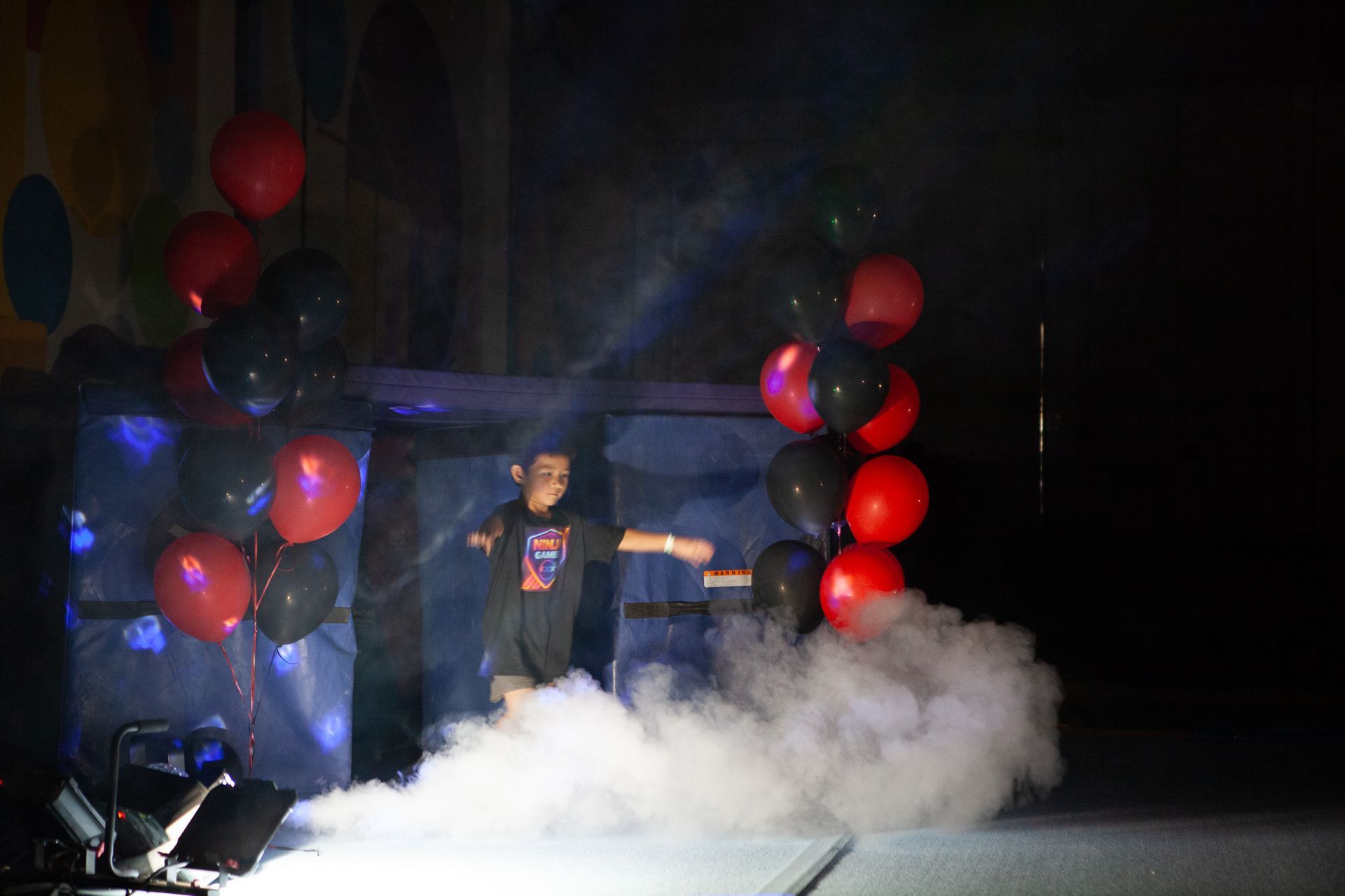 A person on stage with smoke, balloons, and lights, looking out.