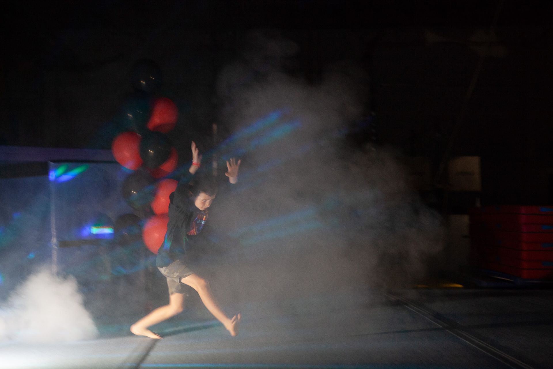 Person running from smoke, holding balloons; stage with blue lights.