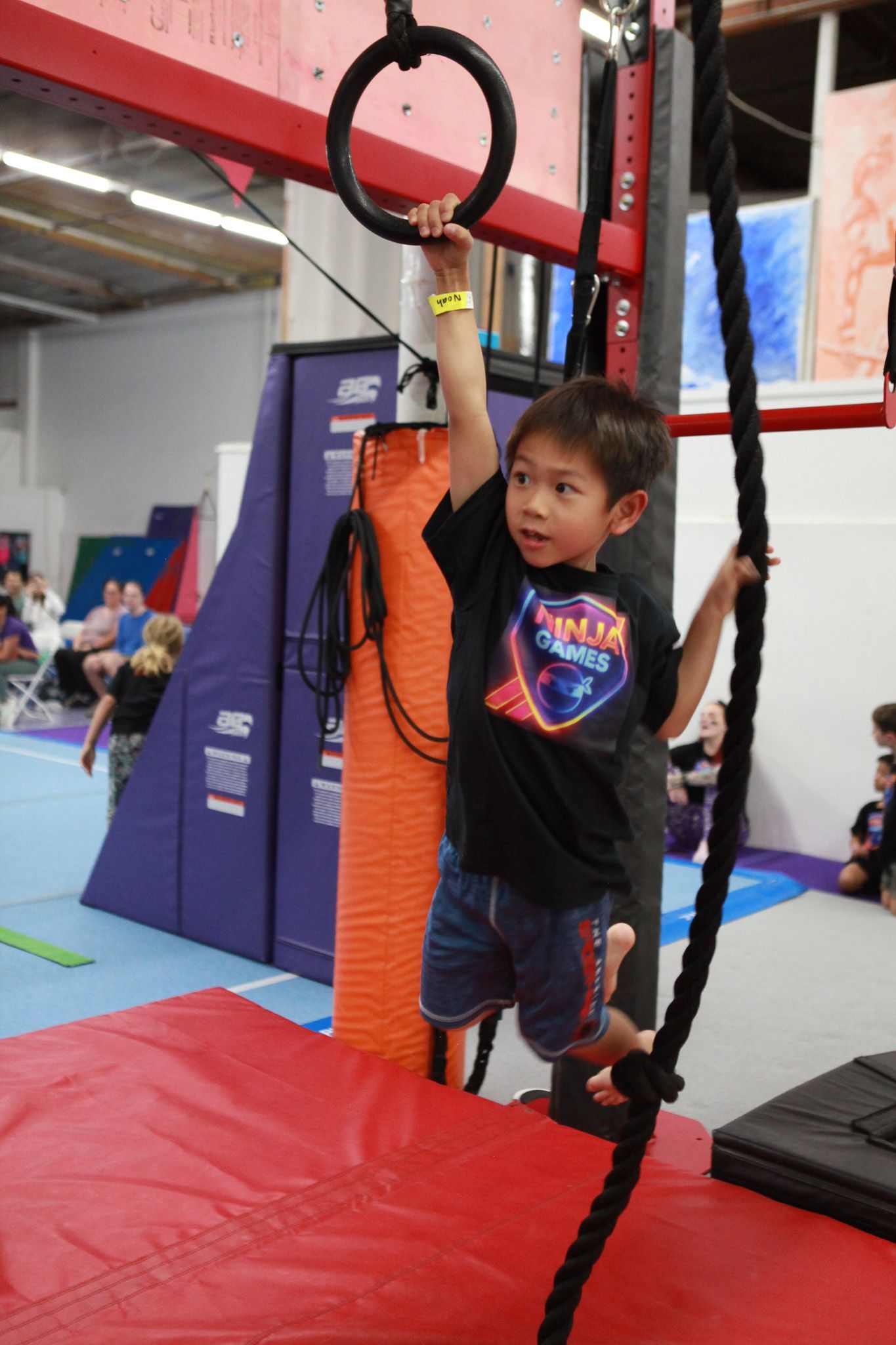 Boy hanging from gymnastic rings and rope in an indoor play gym.