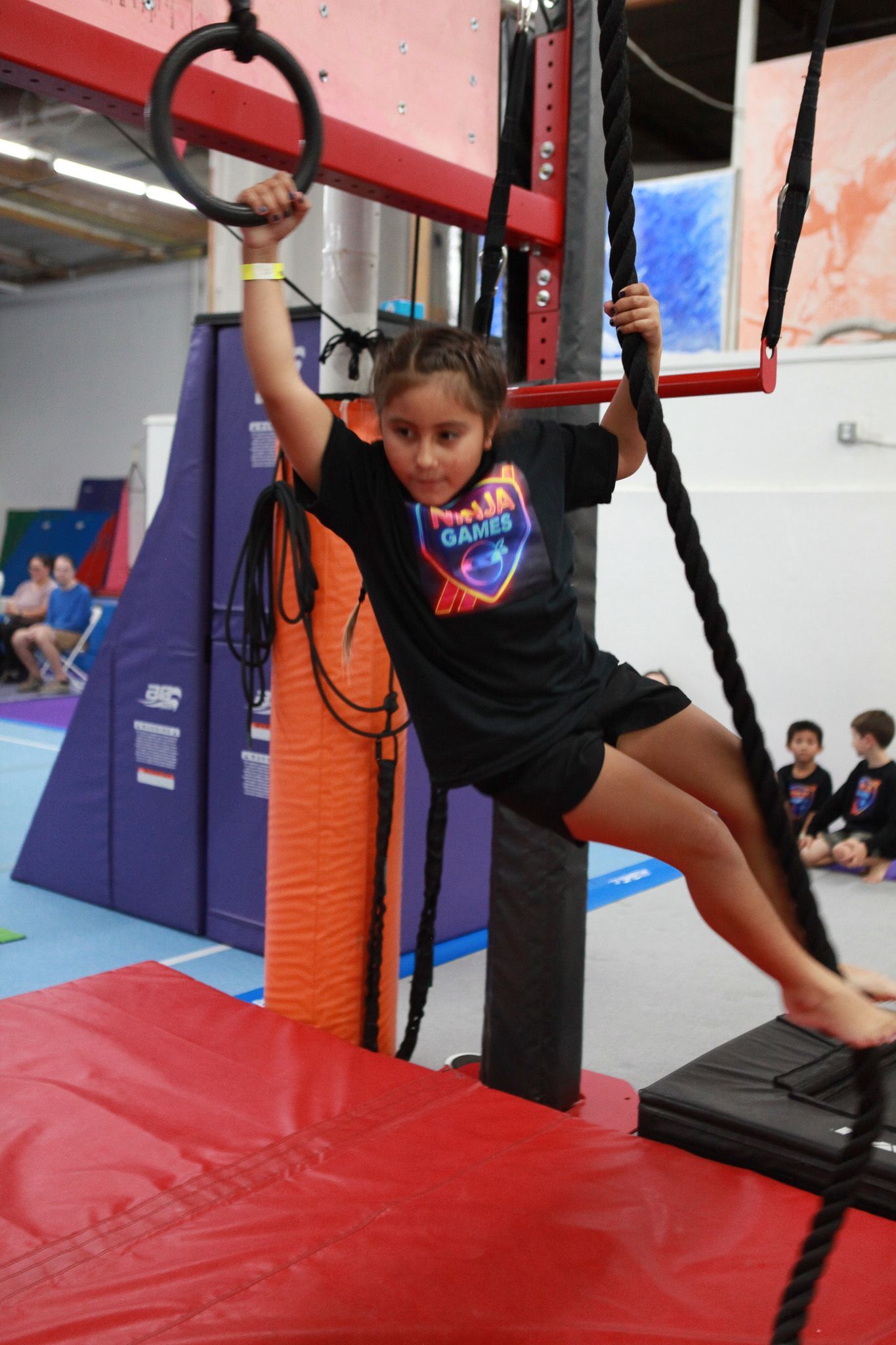 Girl hanging from gymnastics ring and rope, inside a gym.