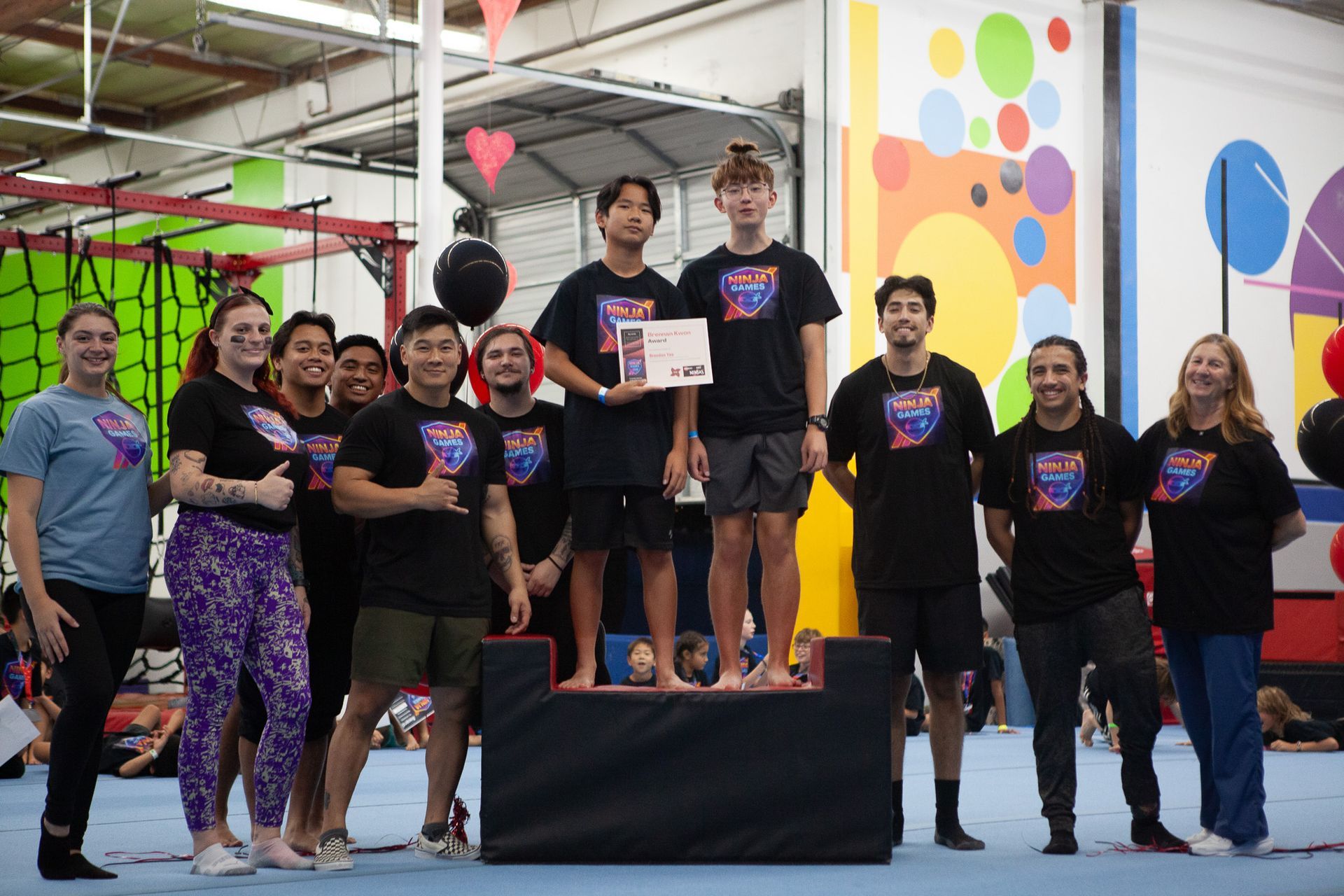 People on podium, some holding awards, indoors, colorful background.