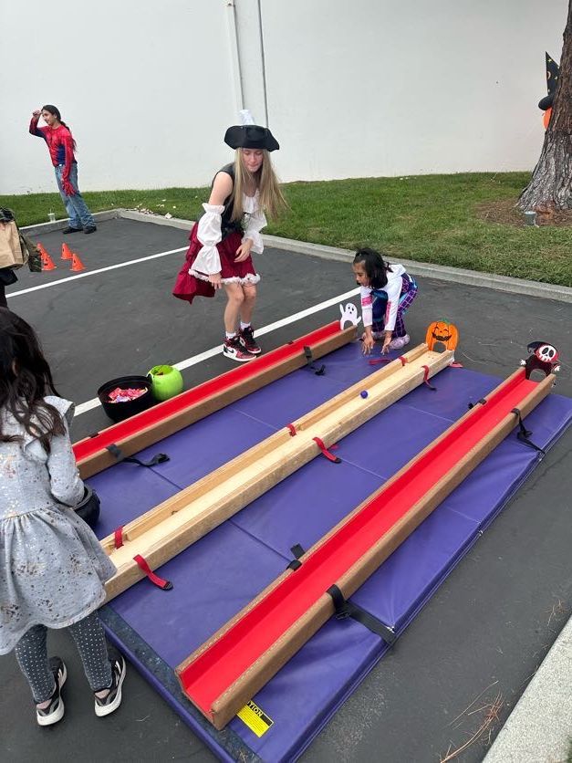 Children in costumes playing a marble race game outdoors.
