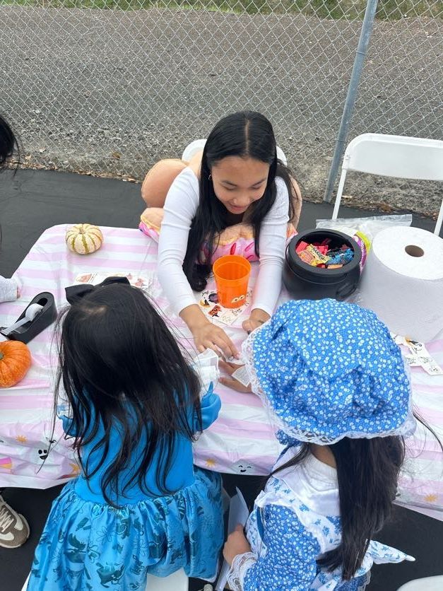 Three children at a table, playing with toys. One child wears a blue bonnet, another a blue dress.
