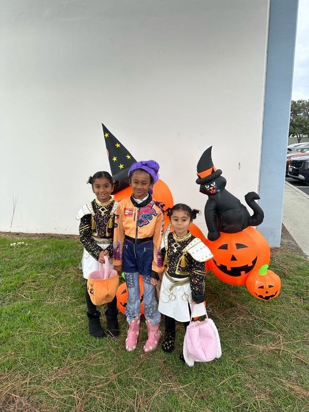 Three children in costumes pose with a Halloween pumpkin display outdoors.