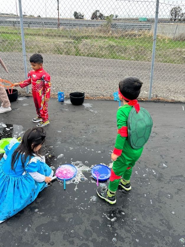 Children in costumes play with bubbles outside.