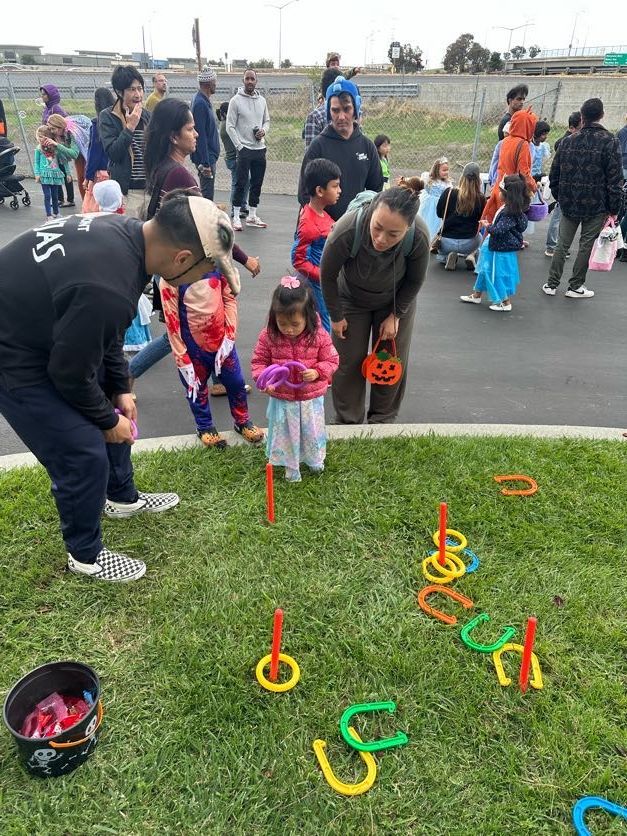 People playing a ring toss game at an outdoor event on grass; children and adults are present.