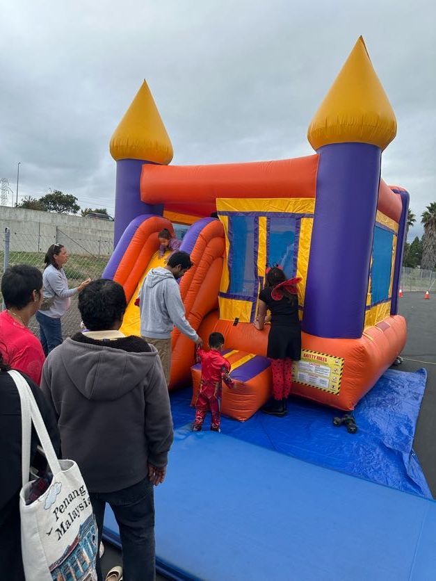 Bouncy castle with children and adults. Red, orange, purple. Outdoor event on a cloudy day.