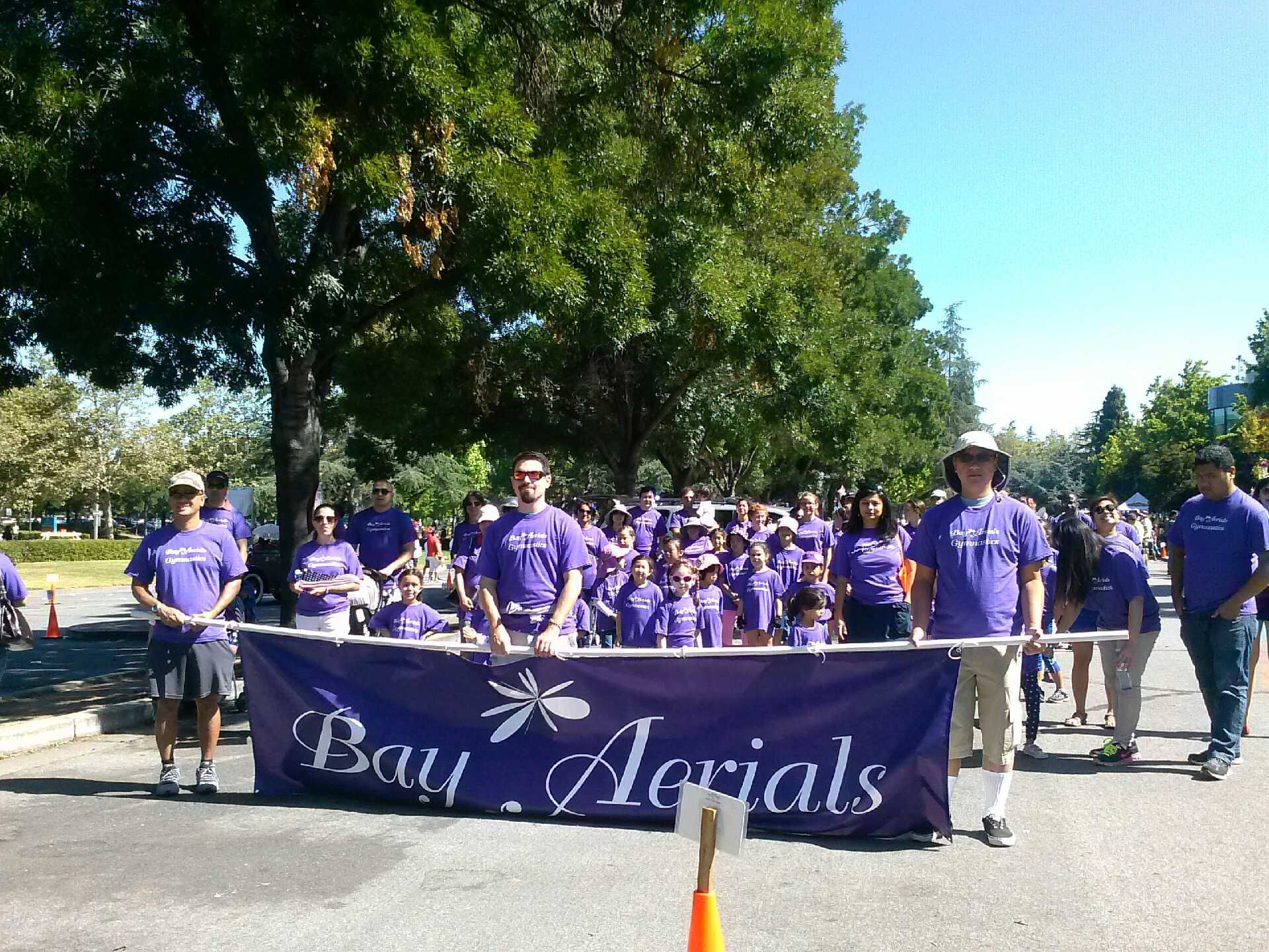 People in purple shirts march in a parade behind a banner for 