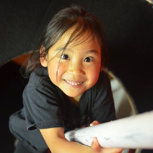 A little girl in a black shirt is smiling and holding a piece of paper