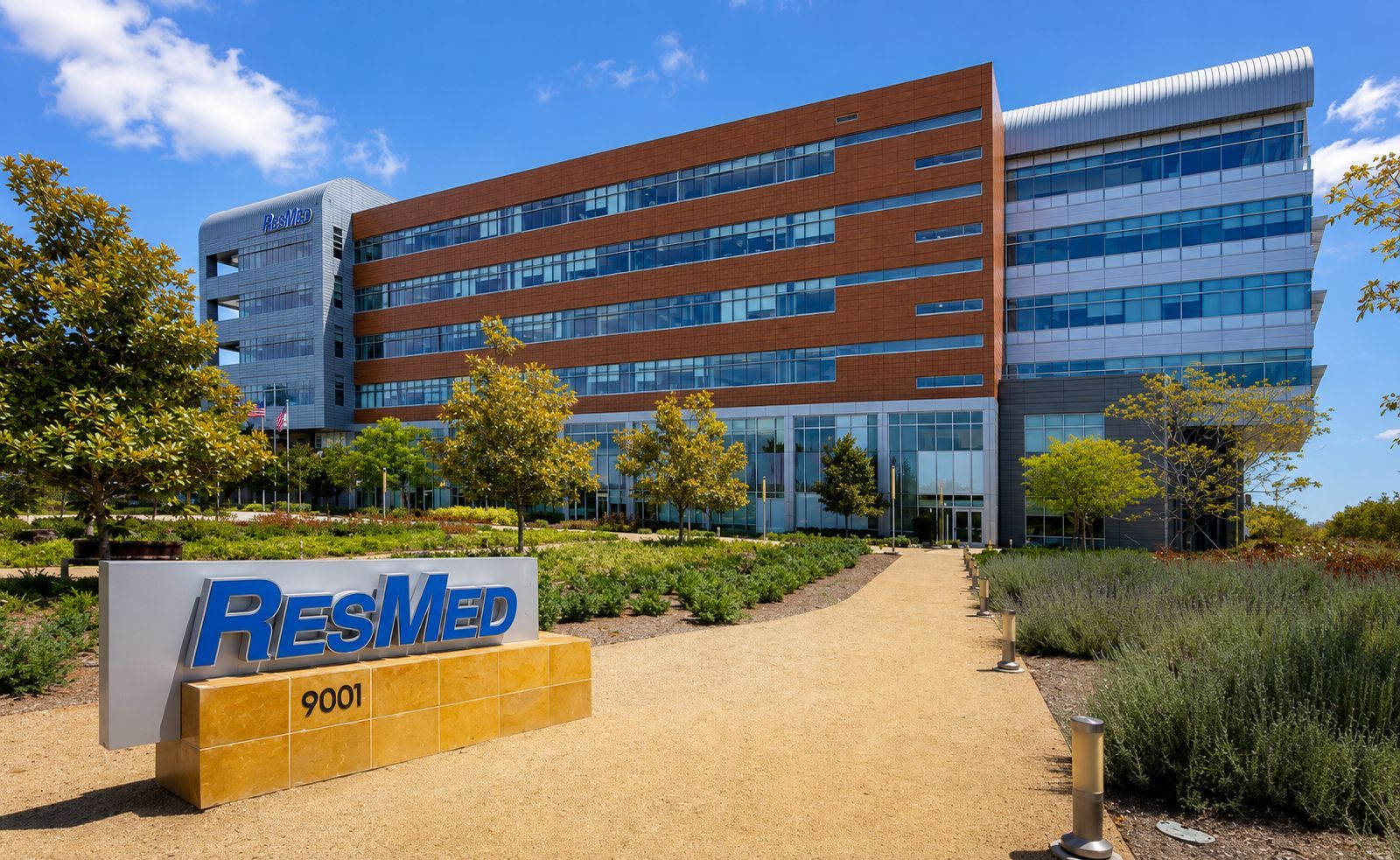 Modern building entrance with a curved canopy, glass facade, and landscaped walkway at sunset