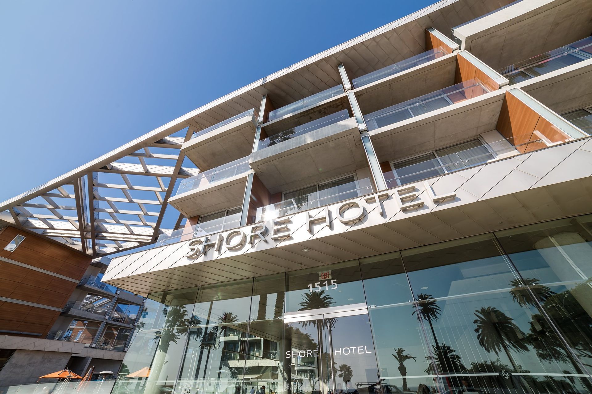 Modern hotel facade with glass entrance and palm trees under a blue sky