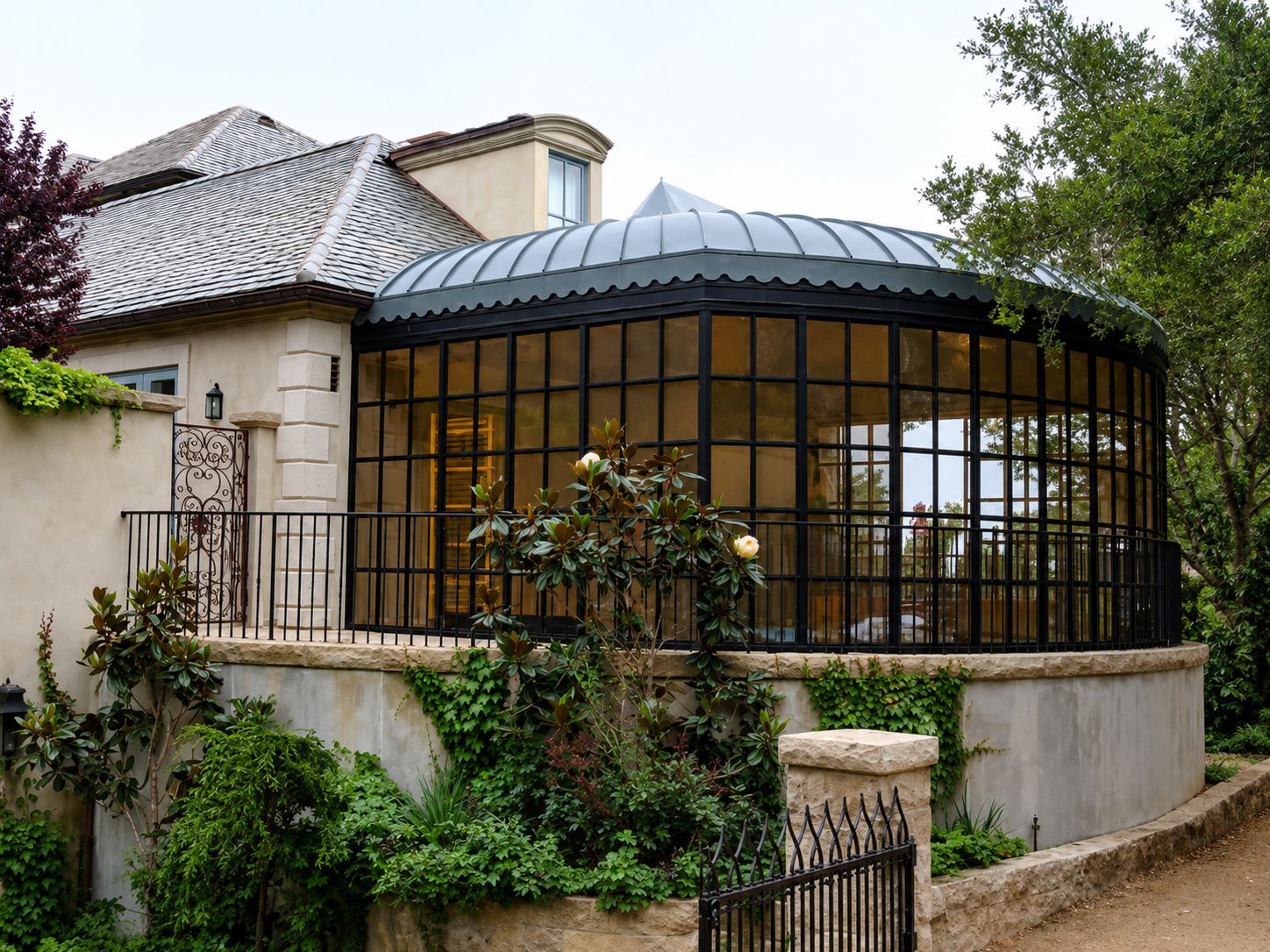 Stone house with a curved glass conservatory and lush greenery in a garden.