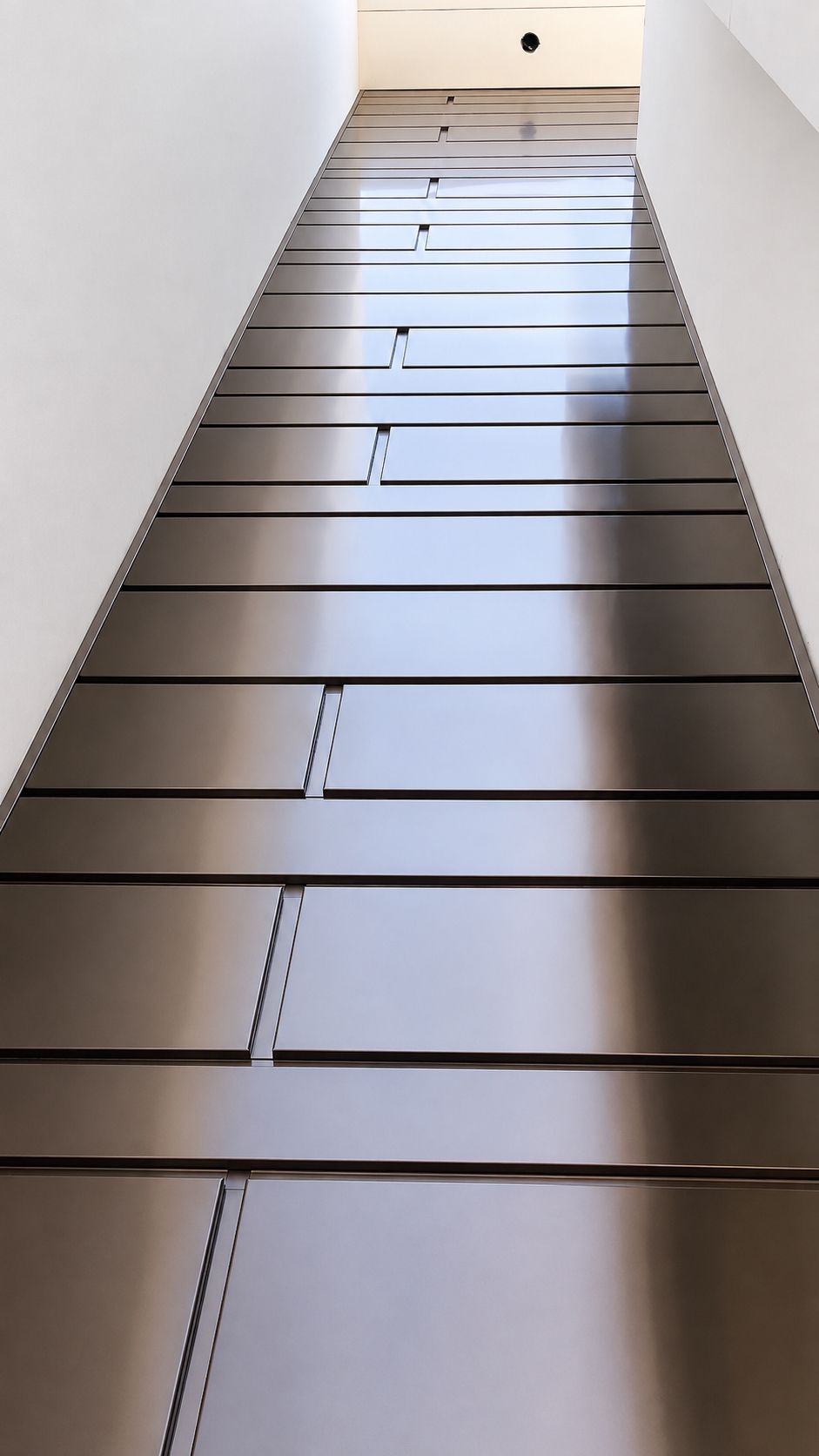Modern staircase with brown steps and white walls, viewed from the bottom looking upward.