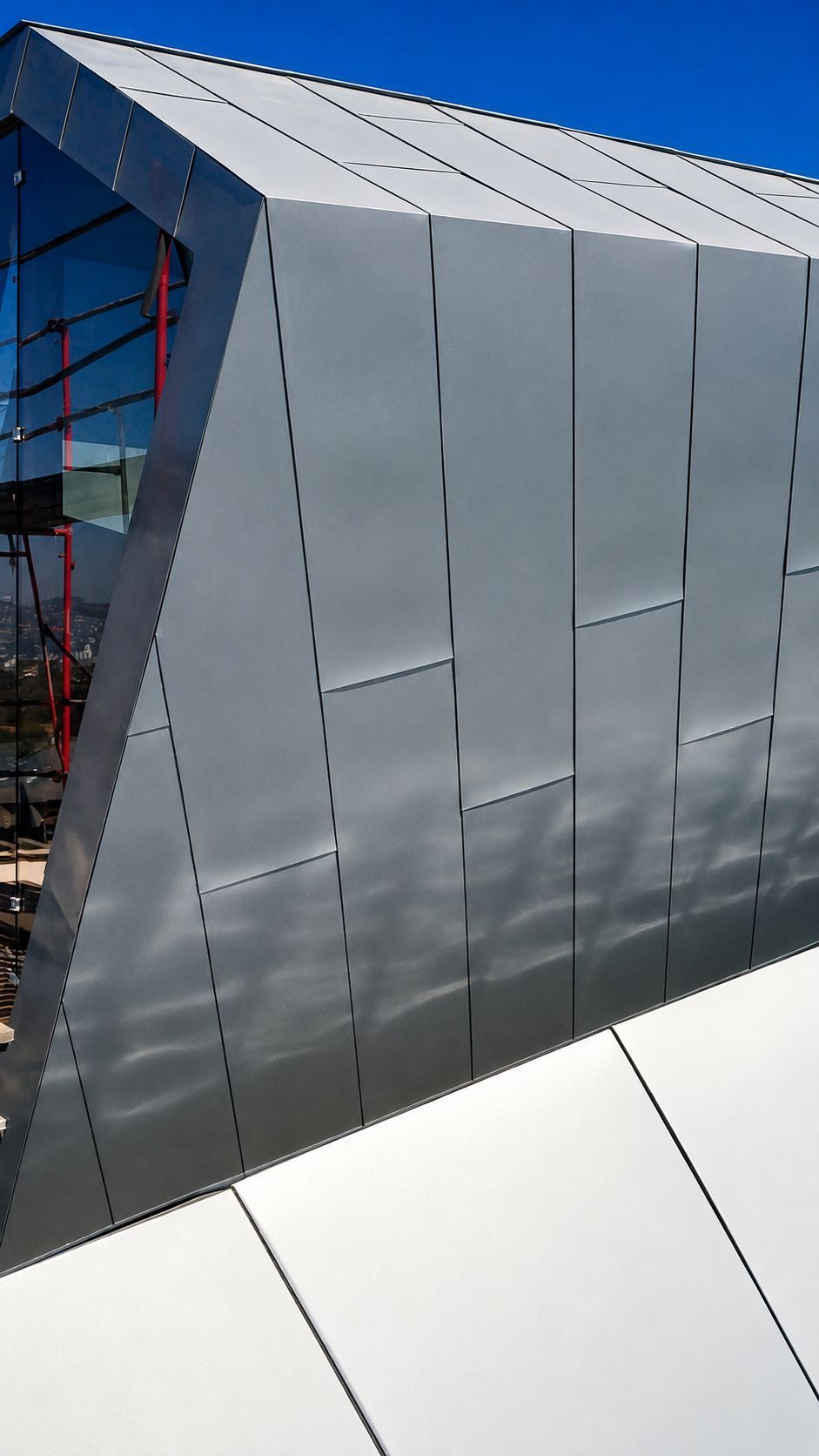 Modern silver metal building facade with angular panels against a blue sky
