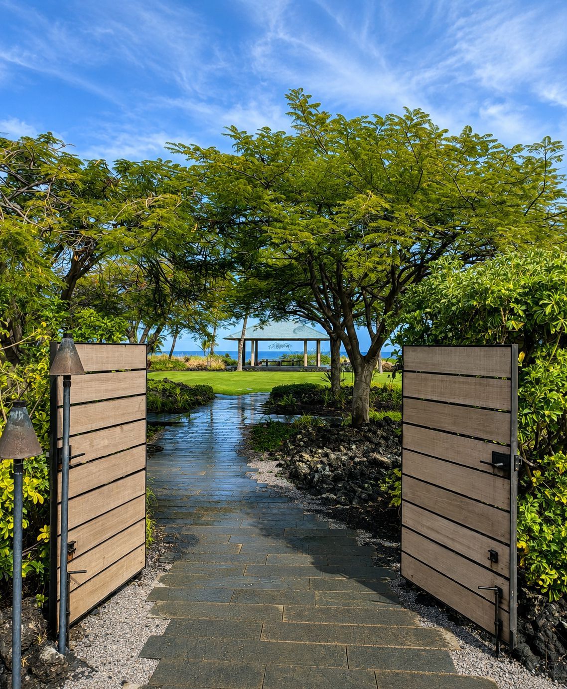 Open gate leading to a sunlit path, trees, and blue water beyond