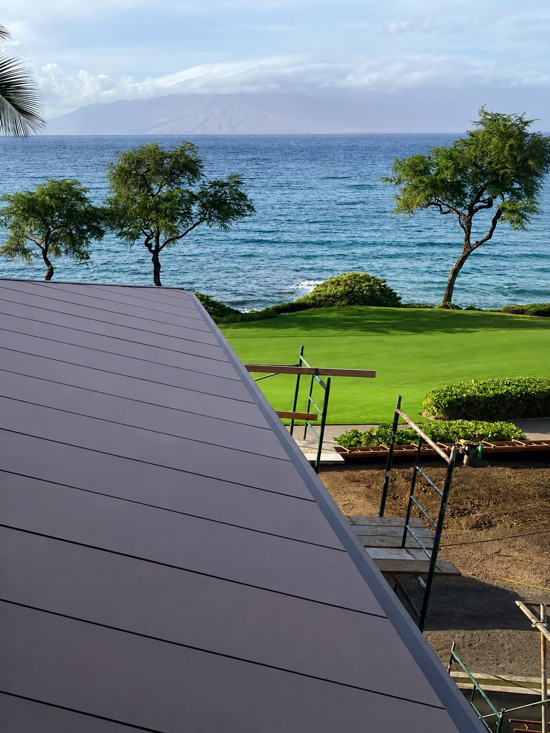 Ocean view with trees, a green lawn, and a gray roof in the foreground