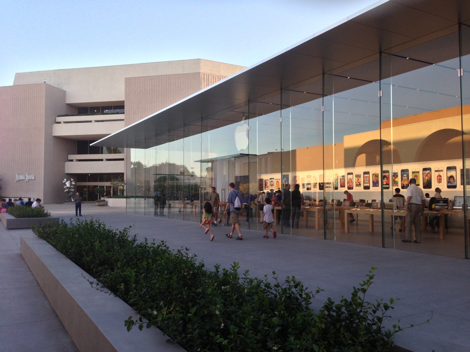 Modern glass-fronted building with people walking along a plaza at sunset