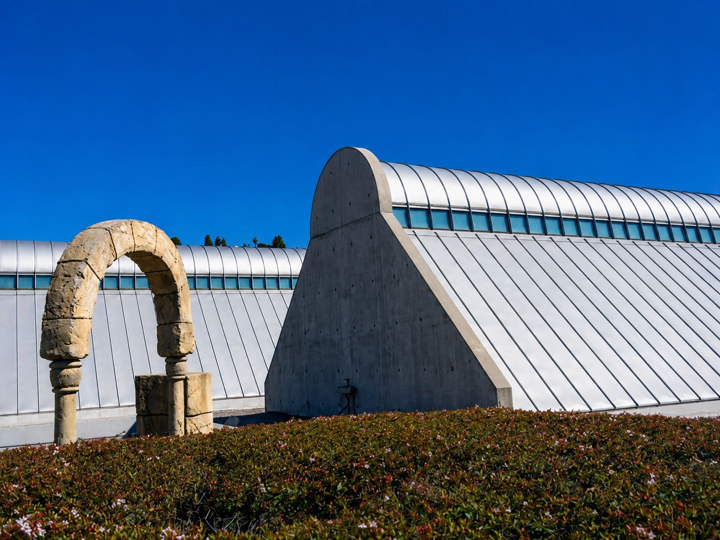 Stone arch sculpture before a modern white building under a clear blue sky