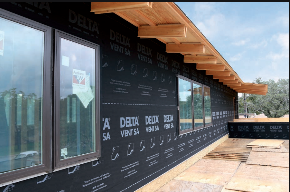 Exterior of a modern building with black facade, large windows, and wooden roof overhang under a blue sky