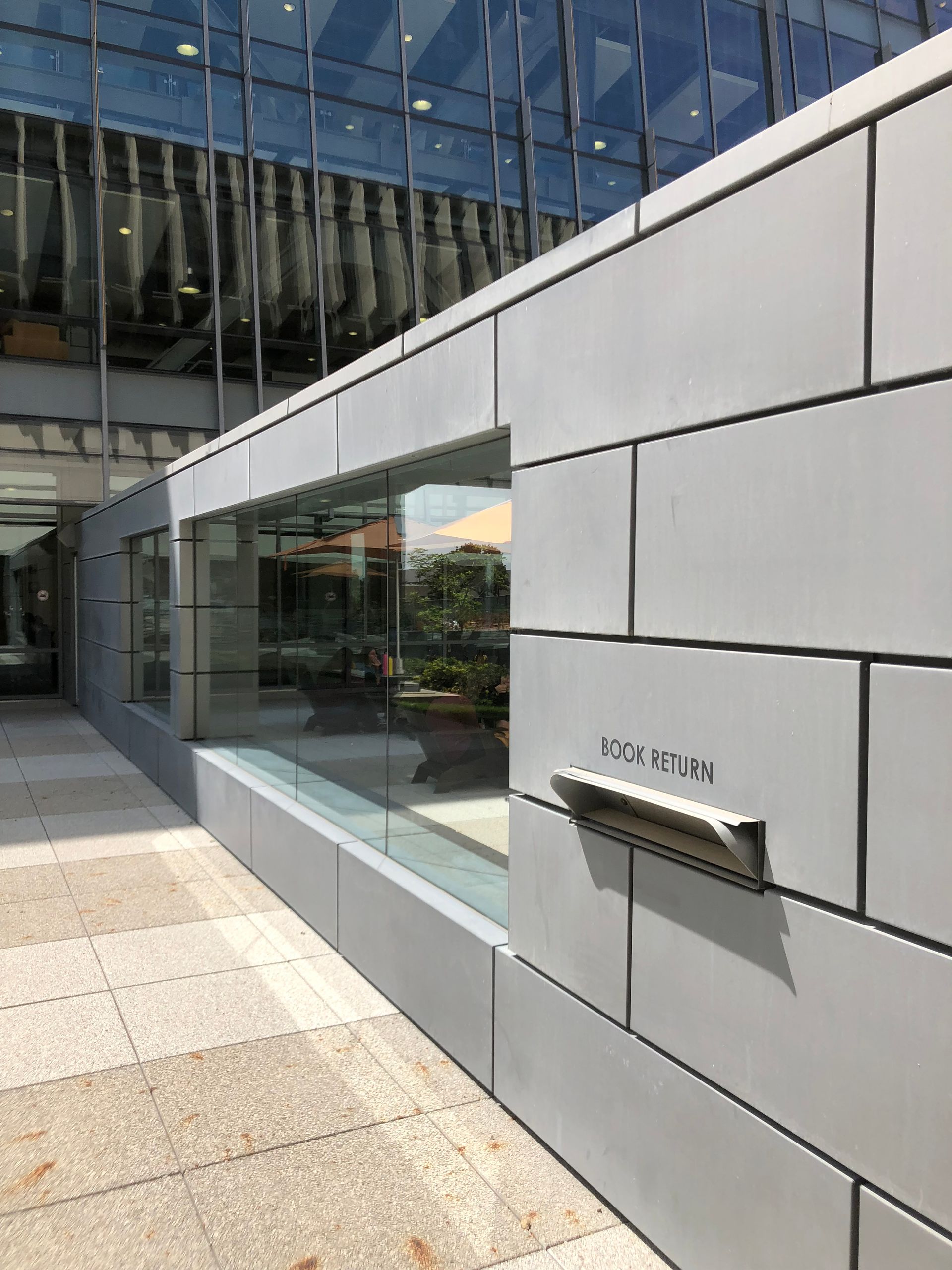 Modern building entrance with white panels, glass windows, and a wall-mounted mailbox in sunlight