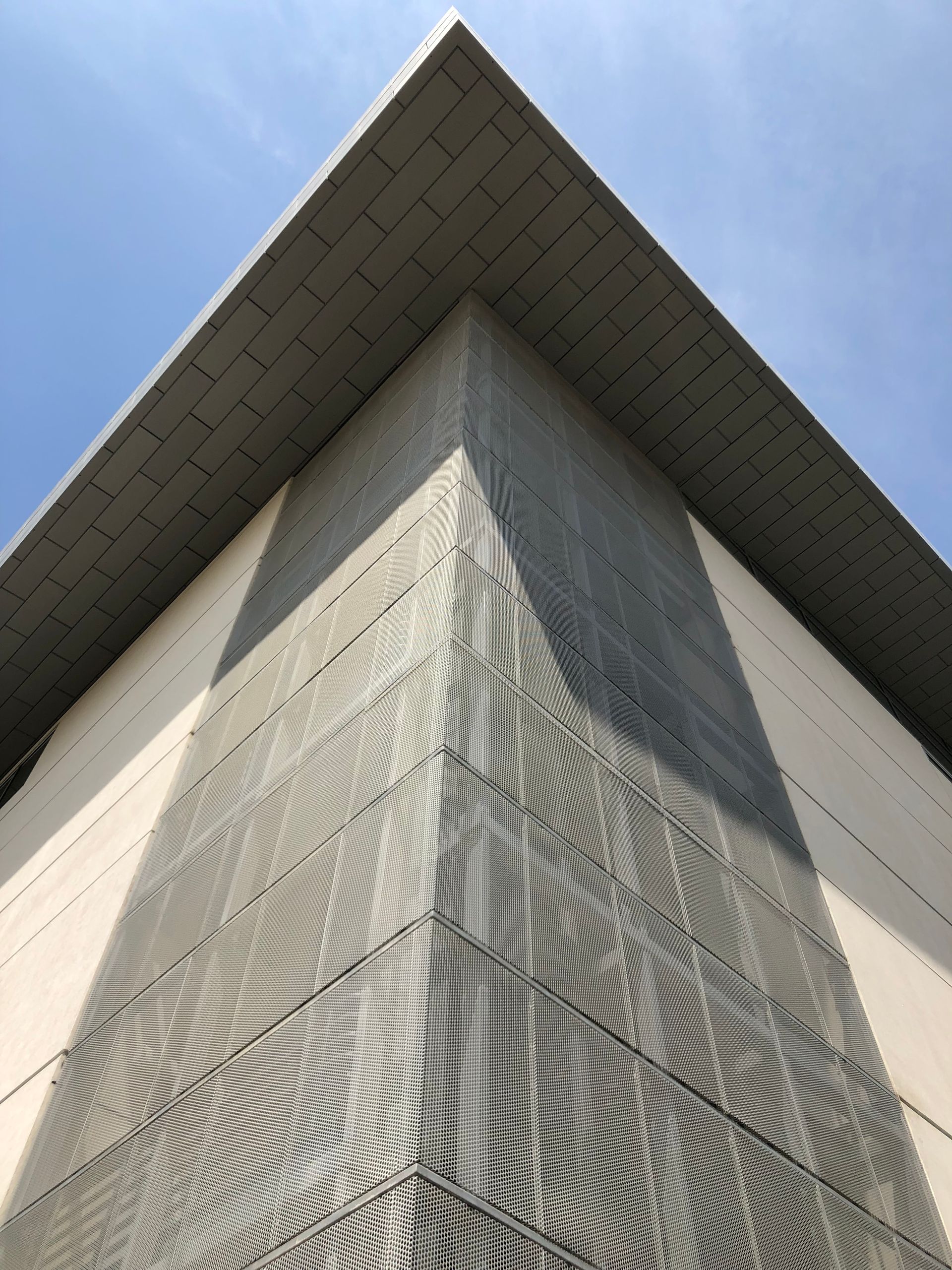 Modern glass-and-steel office building with a large angular canopy against a blue sky