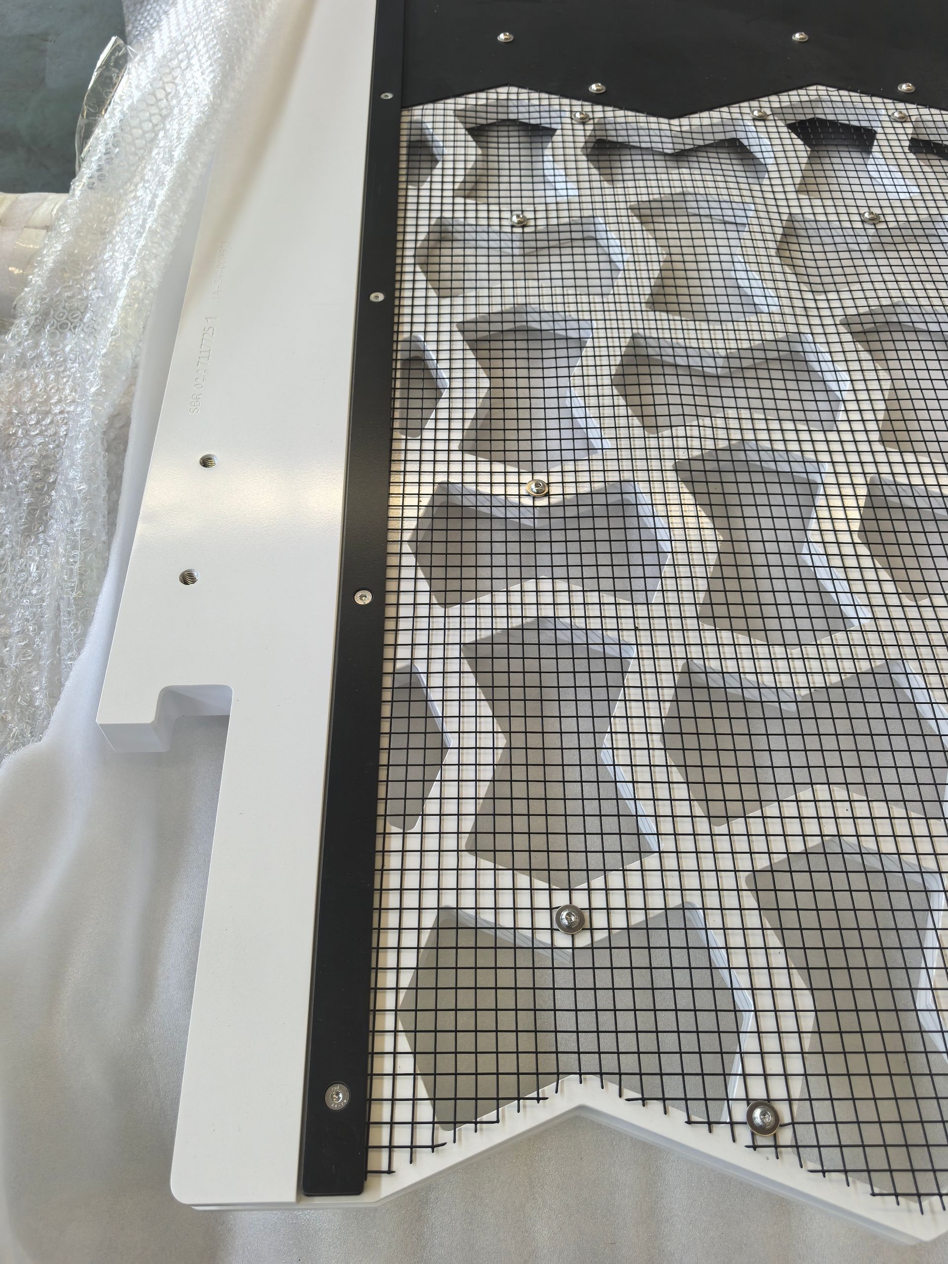 Black grid panel with white fabric or foam padding beside a white plastic packaging insert
