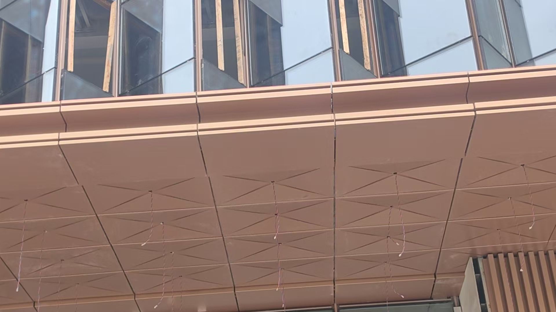 Low-angle view of a modern building facade with reflective windows and a large copper-toned overhang.