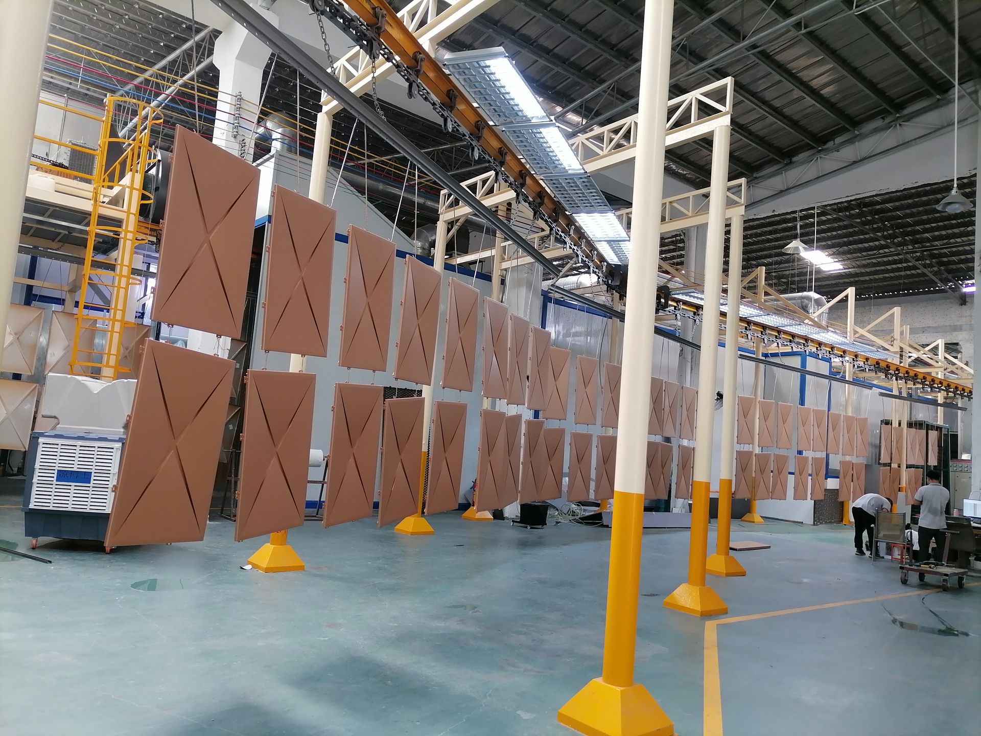 Large industrial workshop with suspended brown panels and yellow support poles in a warehouse-like interior
