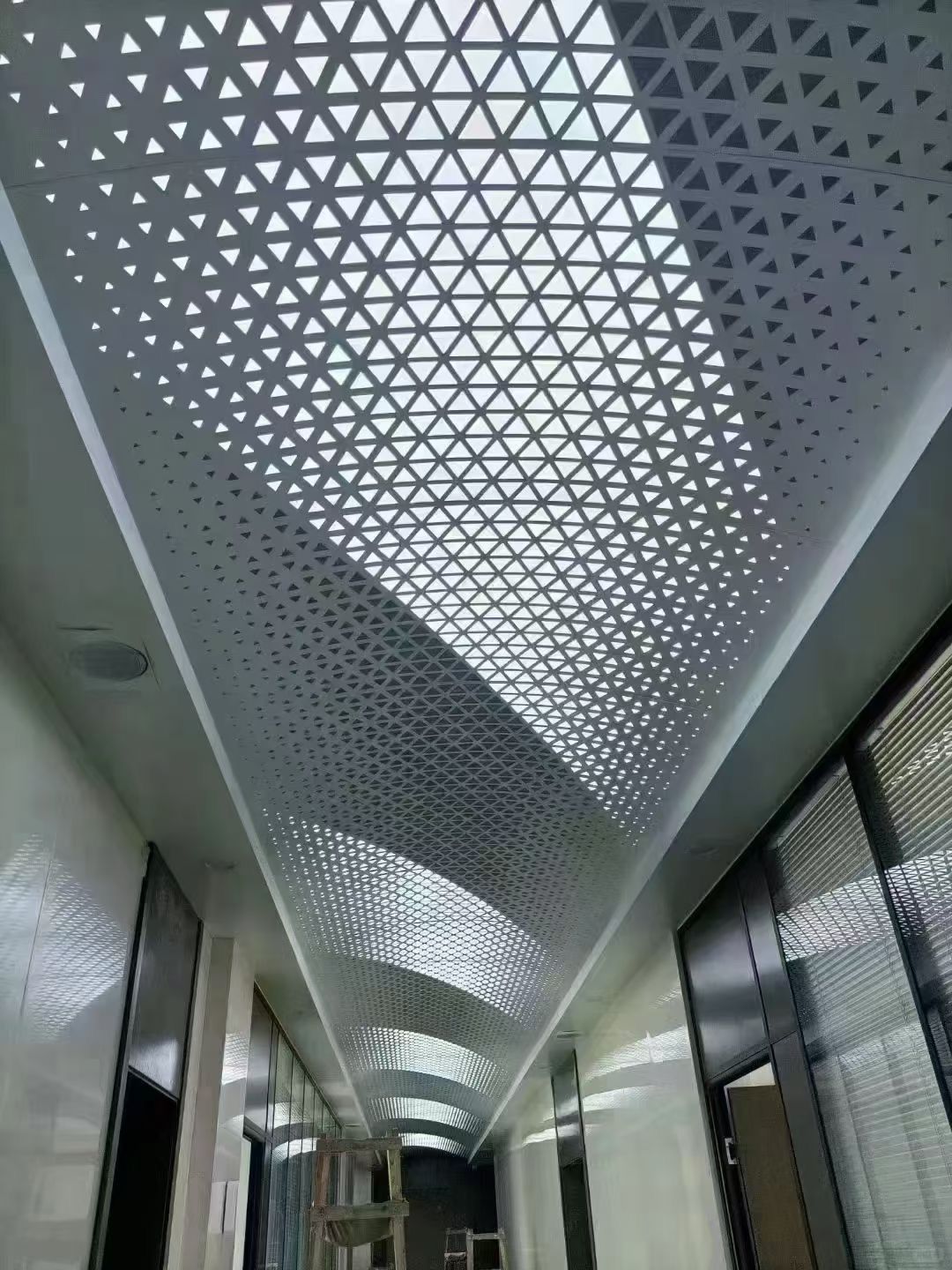 Long hallway with a perforated geometric ceiling and bright skylight panels.