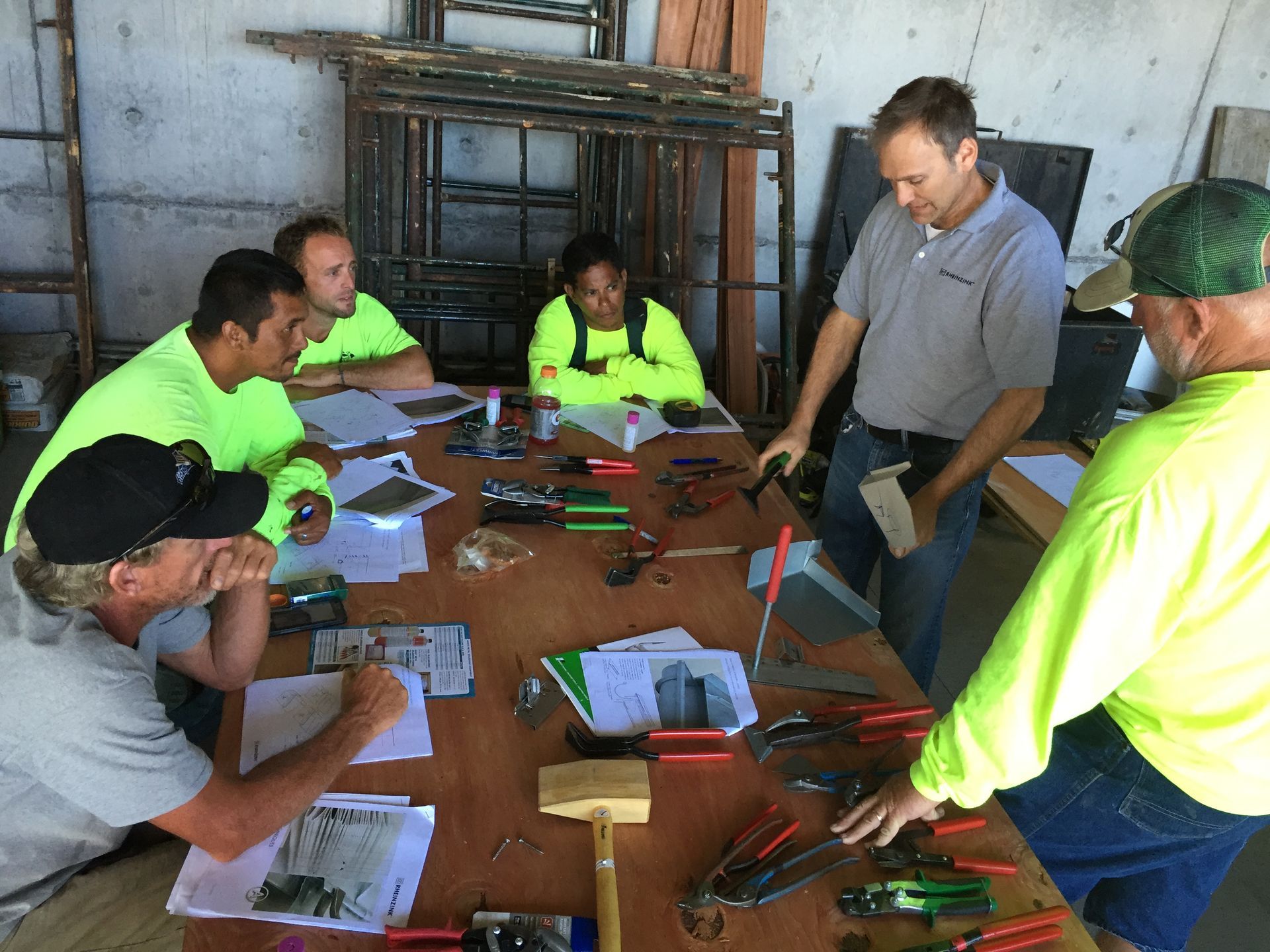 A group in neon shirts and one man stand around a table, reviewing documents and tools in a workshop.