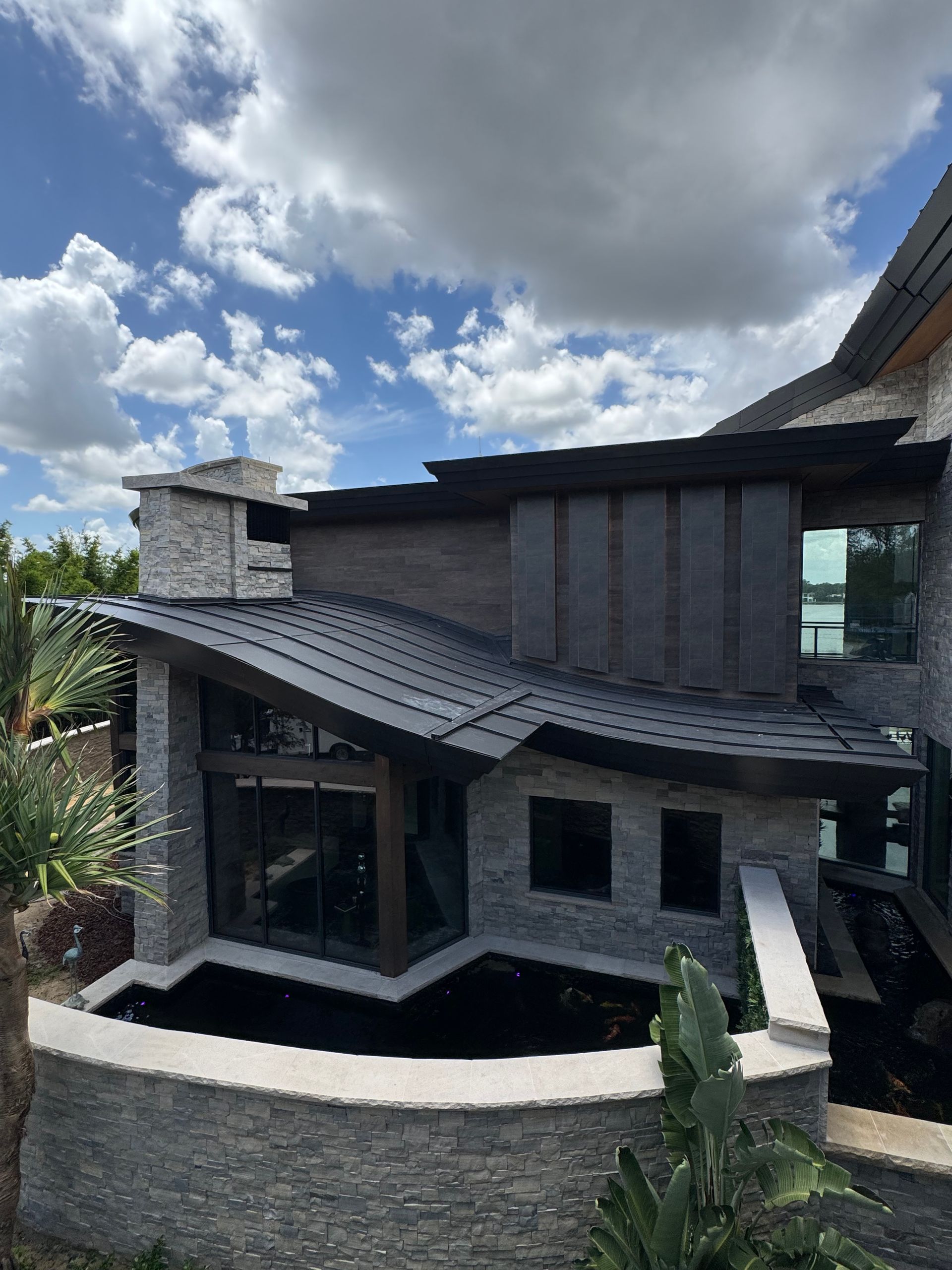 Modern house exterior with dark siding, stone accents, and a curved white wall under a cloudy sky