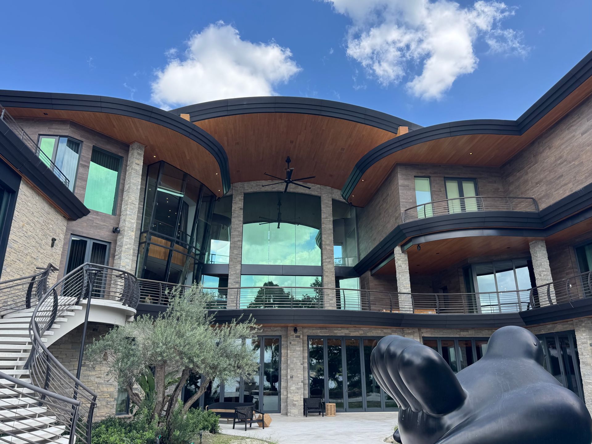 Modern building courtyard with curved balconies, glass facade, and a sculpture in front