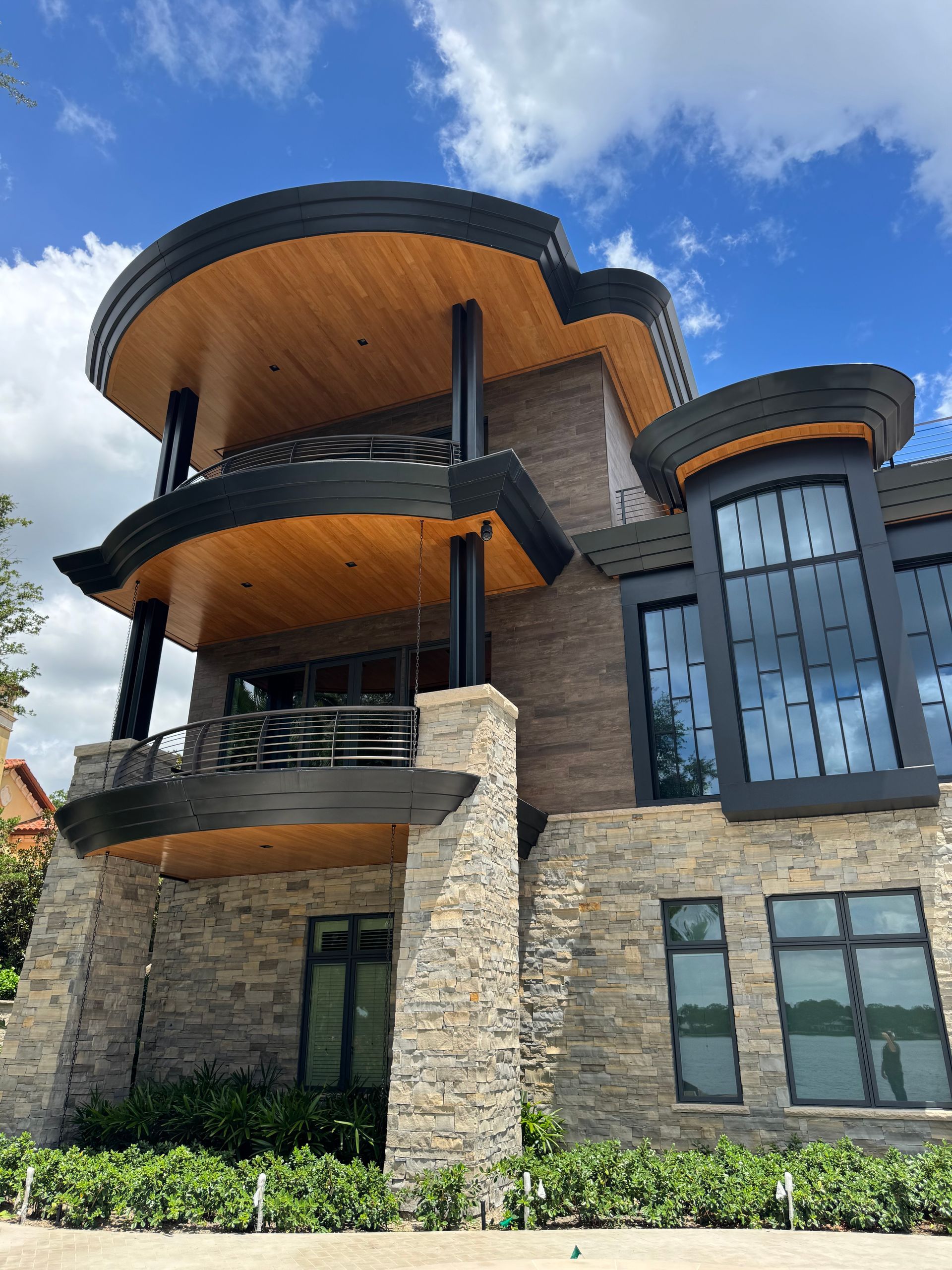 Modern stone-and-glass building with curved balconies and wood soffits under a blue sky