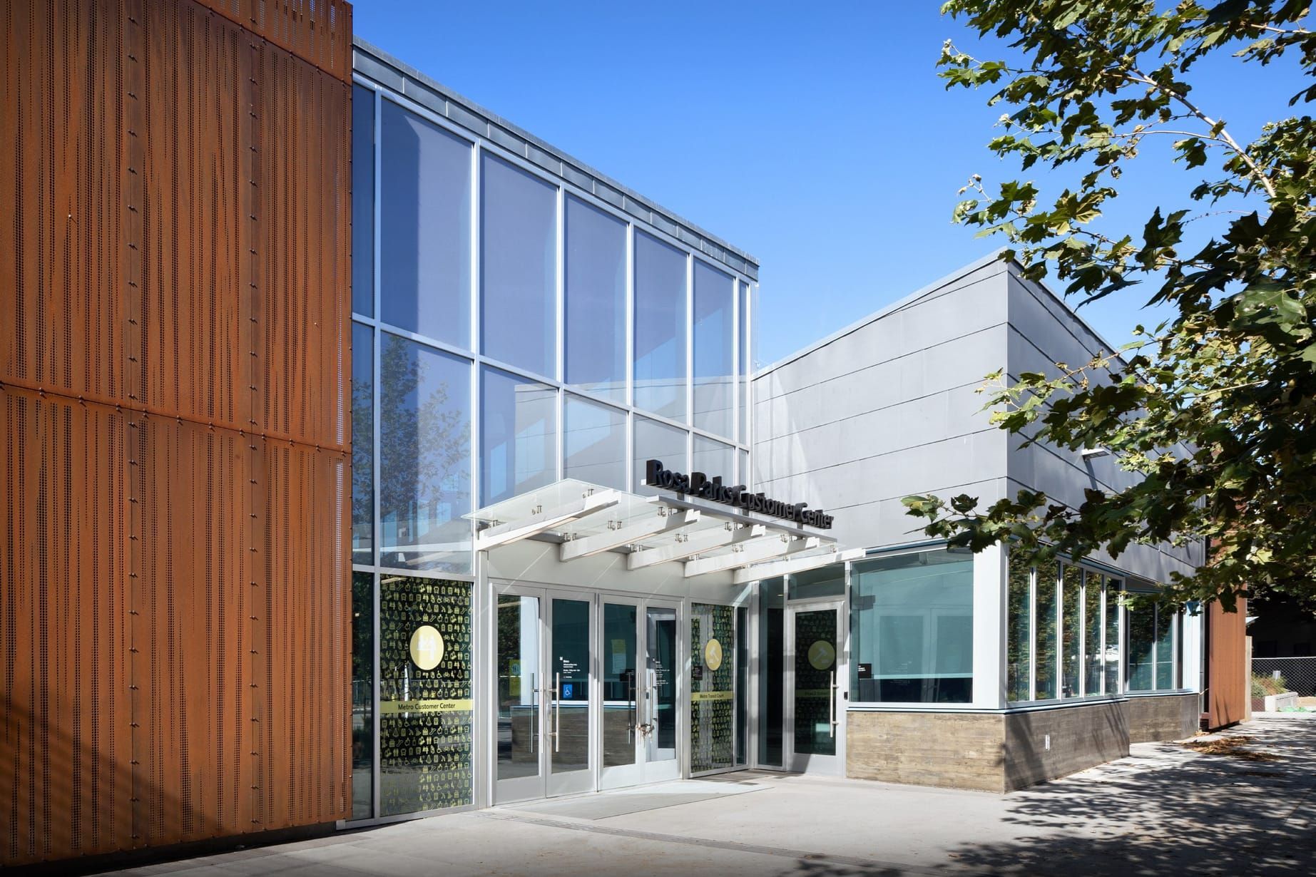 Modern building entrance with a curved canopy, glass facade, and landscaped walkway at sunset