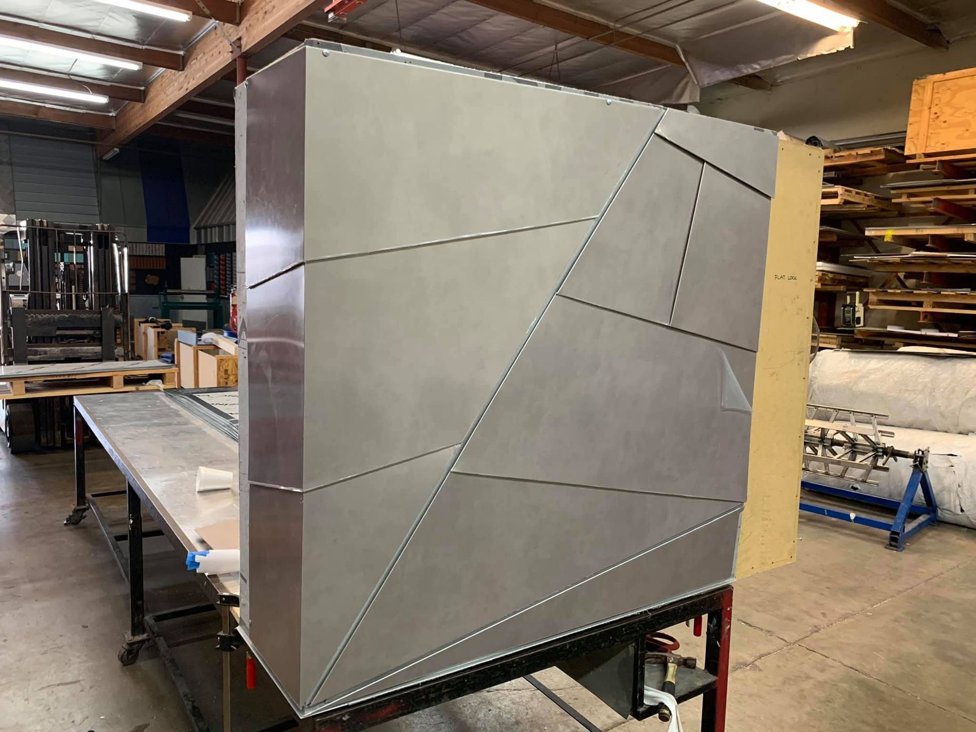 Metal cabinet with faceted gray panels in an industrial workshop, sitting on a cart under construction.