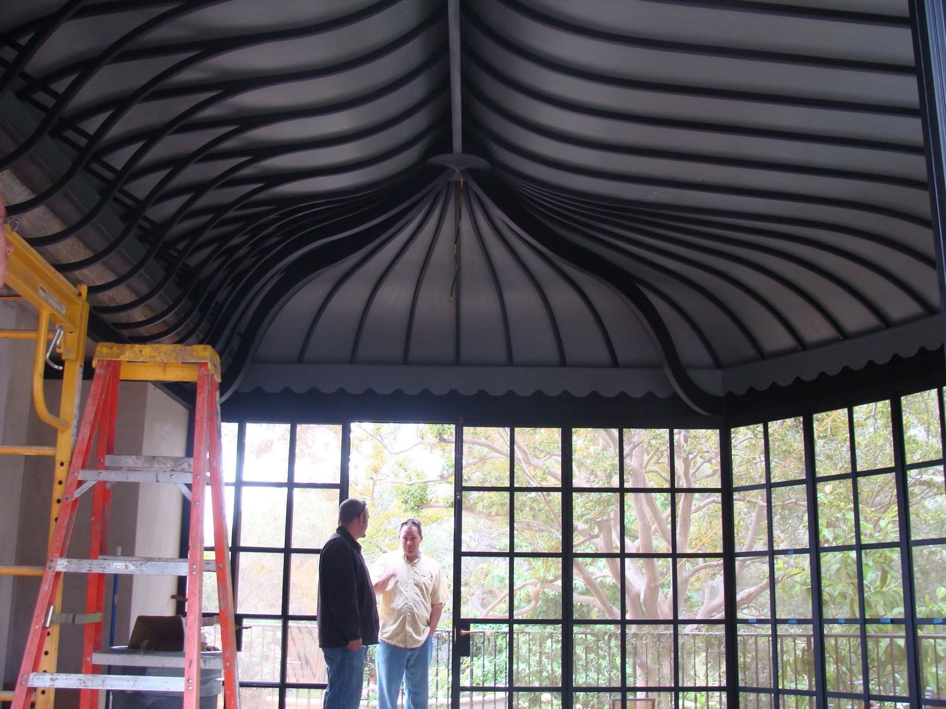 Two people standing in a gazebo-like structure with a curved roof and large windowed walls.