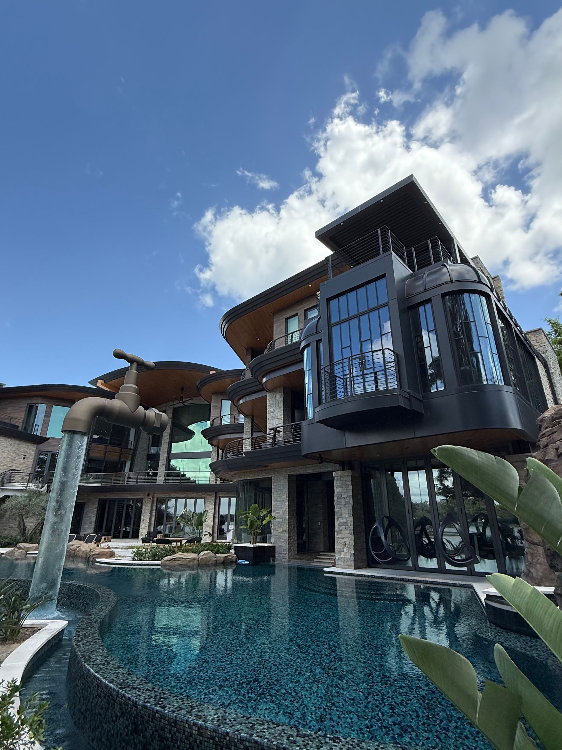 Modern villa with glass balconies beside a blue swimming pool under a bright sky