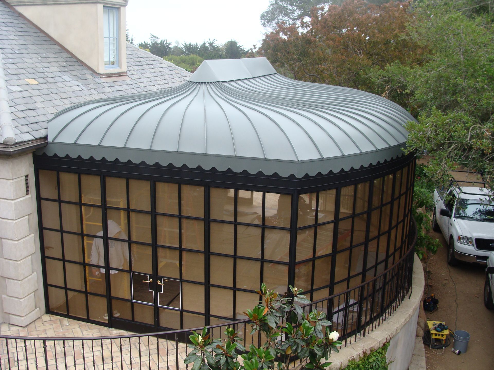 Curved glass sunroom with a green metal roof attached to a brick house, seen from outside