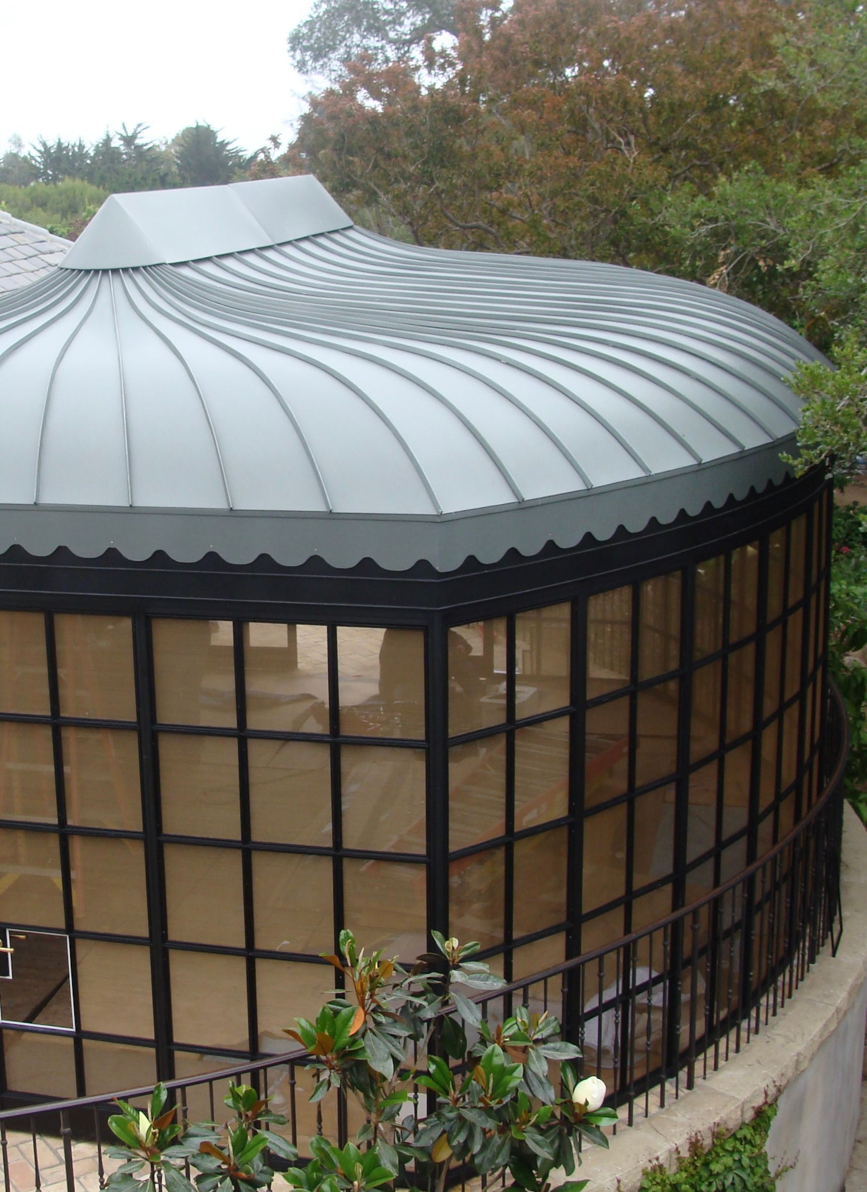 Round glass conservatory with a ribbed gray domed roof and black window frames, surrounded by trees