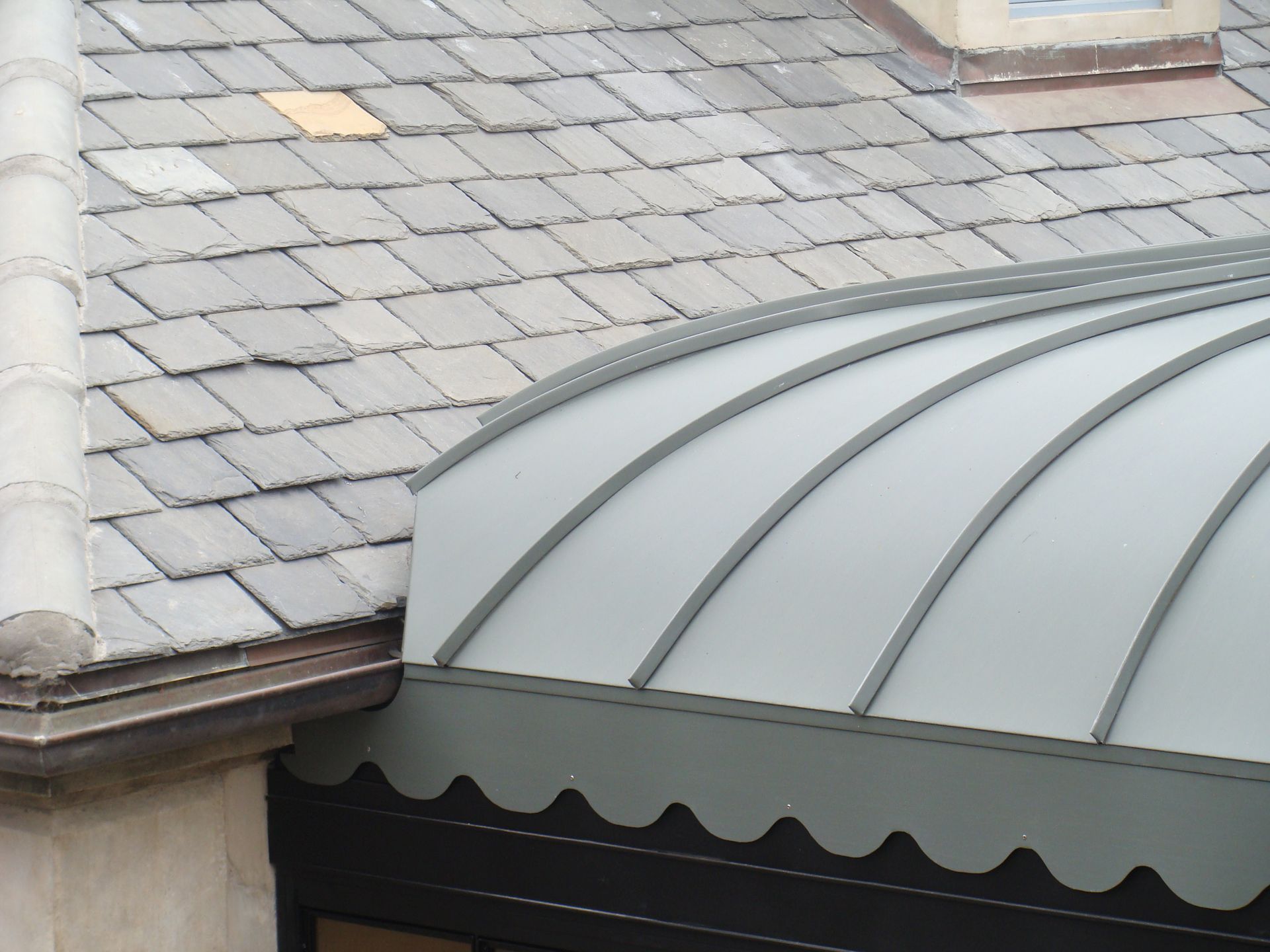 Gray shingled roof with a curved metal awning over a building edge