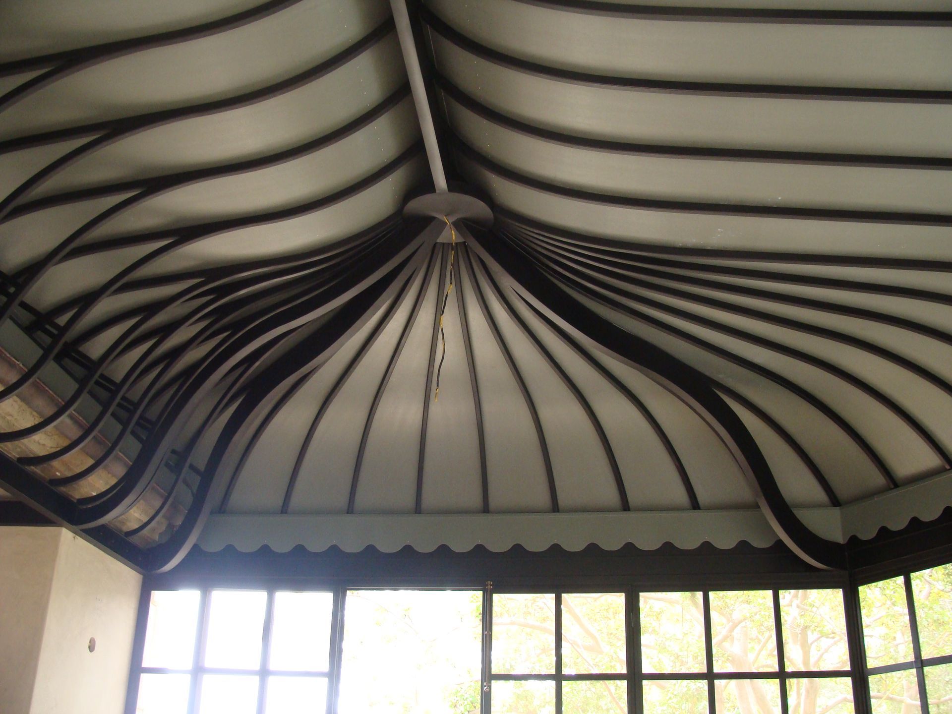 Close-up of a tent-like ceiling with curved dark ribs and a central peak above a bright windowed wall