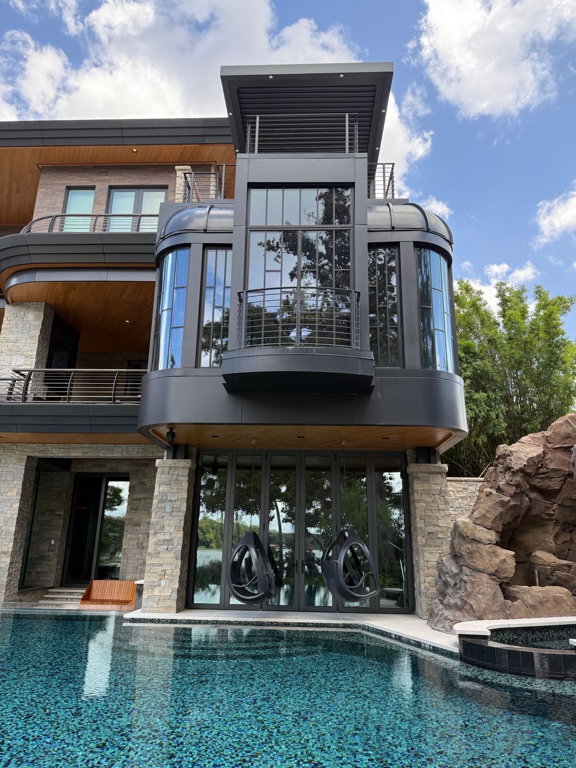 Modern house with glass balcony overlooking a turquoise pool and rocky landscaping