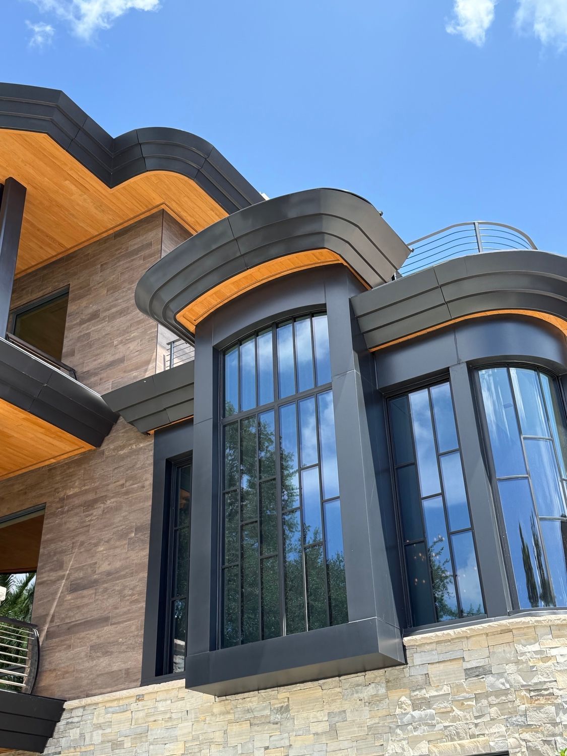 Modern building facade with curved dark gray and orange accents, tall blue-tinted windows, and stone lower walls
