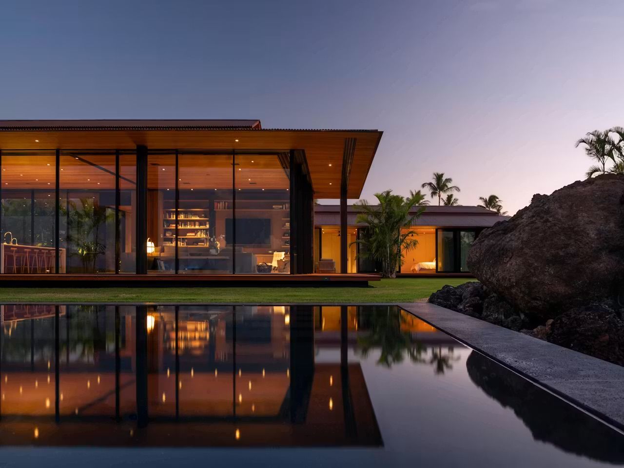 Modern building entrance with a curved canopy, glass facade, and landscaped walkway at sunset