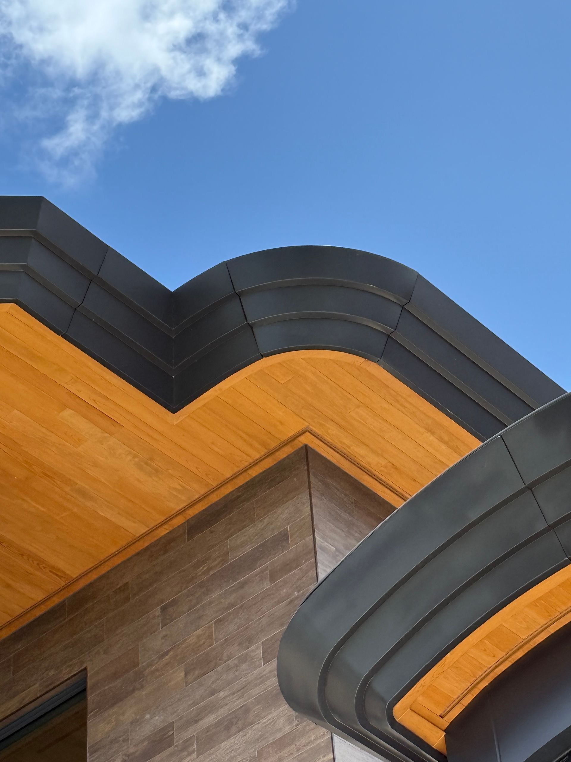 Close-up of modern building roof with orange and dark gray angular panels against a blue sky