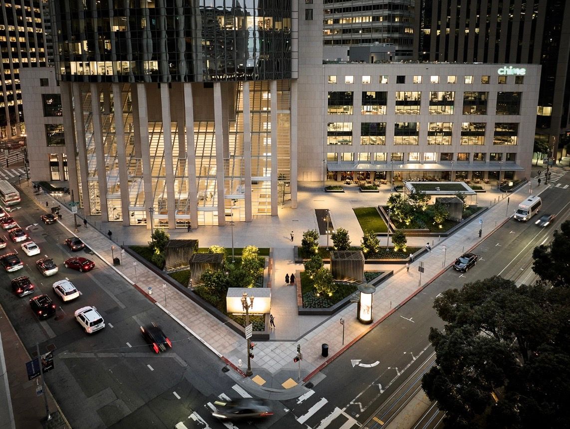 Aerial view of a lit city intersection beside a modern office complex at dusk